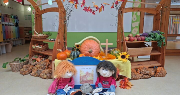 Stand mit Obst und Gemüse, vorne ein Kreuz, davor zwei Handpuppen